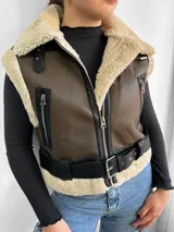 Chaleco marrón de cuero sintético con interior de piel sintética color beige. Tiene cierre frontal con cremallera, bolsillos laterales con cremallera y cinturón con hebilla.