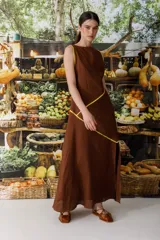 Vestido largo de lino marrón con cuello semi-bote, sin mangas y aberturas laterales en el bajo. Cuenta con detalles de líneas en color amarillo a contratono que recorren la prenda de forma diagonal.