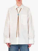 Camisa blanca de algodón con cuello clásico, manga larga con puños abotonados, cierre frontal con botones y bolsillo en el pecho. Incluye un bolo tie con cordón de cuero marrón y dije turquesa.