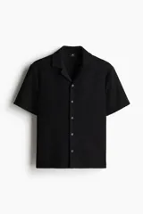 Camisa negra de manga corta con cuello abierto (tipo resort) y tapeta lisa con botones. Presenta una textura rizada o bouclé en toda la prenda.