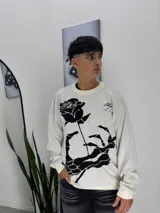Sweater de punto color crema con diseño gráfico en negro que representa una mano esquelética sosteniendo una rosa. Presenta cuello redondo y puños acanalados.