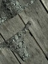 Bikini de dos piezas color marrón, con corpiño triangular fijo con corte bajo el busto, breteles regulables con hebilla y almohadillas desmontables. La bombacha es vedetina con frunce elástico en los costados.