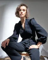 Mono largo negro de acetato con mangas largas abullonadas con elástico en los puños, detalle de raso en hombros y cinturón, escote en V regulable con cierre invisible y textura plisada artesanal en el frente superior.