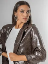 Blazer de mujer color marrón chocolate, confeccionado en ecocuero texturizado con acabado acharolado. Es forrado y presenta un corte estructurado con solapas y bolsillos frontales.