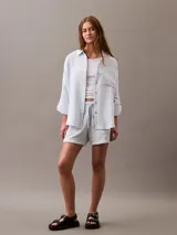 Camisa celeste de gasa doble, con cuello clásico, cierre frontal con botones, bolsillo de parche en el pecho y mangas largas con solapa enrollable.