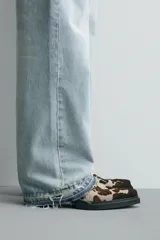 Zueco de piel con pelo, con estampado animal print tipo vaca en tonos marrones y beige. Presenta una suela de goma a contraste con un ligero tacón cuadrado y punta redondeada.