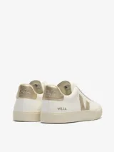 Championes Veja modelo Campo, de diseño minimalista en color blanco con detalles en dorado metalizado en el logo lateral y el talón. Presentan suela de caucho en tono crema y cierre mediante cordones.
