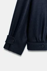 Chaqueta bomber de corte holgado confeccionada en tejido con lana, color azul marino. Presenta cuello subido, cierre frontal con cremallera metálica, bolsillos delanteros y detalle de trabillas con botones metálicos en el ruedo.