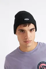 Gorro de invierno negro tejido en canalé, con vuelta y parche frontal con el logo de la marca en blanco y negro.