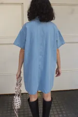 Vestido camisero celeste de denim con botones frontales, mangas cortas, cuello camisero y bolsillos cuadrados.