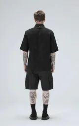 Camisa negra de manga corta con cuello camisero y botones frontales. La tela presenta un patrón texturizado en relieve de motivos florales o abstractos.