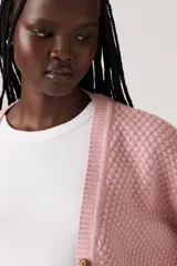 Cardigan de punto color rosado, con escote en V, cierre frontal con botones marrones y mangas largas con puños acanalados.