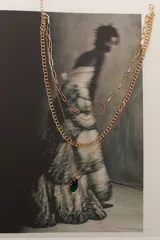 Colgante dorado de tres cadenas de diferentes grosores y diseños. La cadena más larga tiene dos dijes circulares unidos. La cadena más corta tiene un dije de piedra facetada color verde oscuro.