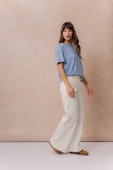 Pantalón jean de tiro alto y corte wide leg, color off white. Presenta un diseño minimalista con bolsillos funcionales, cierre frontal con botón y detalles metálicos plateados.