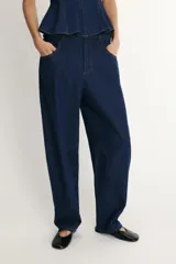 Pantalón de jean azul oscuro con corte tipo ballon, tiro alto, cierre frontal con cremallera y botón metálico, bolsillos delanteros y traseros.