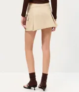 Short pollera beige de sarga con bolsillos cargo laterales y solapa, cintura ancha, pliegues delanteros y cierre frontal discreto.