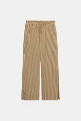 Pantalón de tiro medio con diseño de rayas verticales en tonos beige y marrón. Presenta una cintura elástica ajustable con cordones, bolsillos laterales ocultos y corte de pierna recta con aberturas en el bajo.