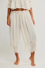 Pantalón lounge de tiro medio y largo cropped, confeccionado en tela liviana con cintura fruncida y lazo ajustable. Presenta diseño abullonado en las piernas y detalle de encaje translúcido en el ruedo.