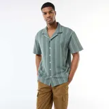 Camisa de manga corta de color verde con diseño de rayas verticales blancas, cuello tipo cubano y cierre frontal con botones.