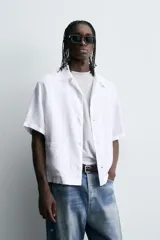 Camisa de manga corta confeccionada en tejido de cáñamo, con calce relajado. Presenta cuello solapa, cierre frontal con botones y dos bolsillos de plastrón en la parte inferior delantera.