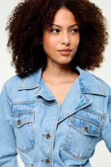 Vestido camisero corto confeccionado en denim azul claro, con cuello camisero, cierre frontal de botones metálicos, bolsillos frontales con solapa en el pecho y diseño entallado en la cintura.