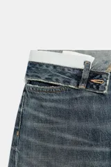 Jeans de mezclilla de tiro medio, corte wide leg y diseño relaxed. Presenta detalles rotos y desgastados en las piernas, y una cinturilla doblada superpuesta con trabillas y cierre frontal con cremallera y botón metálico.