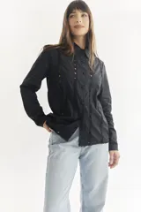 Camisa negra de manga larga con cuello clásico y cierre frontal con botones. Presenta detalles de encaje en el frente, los hombros y los puños.
