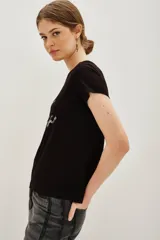 Remera de viscosa color negro, de corte clásico y manga corta, con estampa frontal de texto bordada en lentejuelas plateadas.