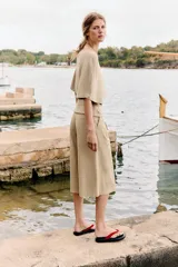Top de punto color beige con cuello barco y mangas cortas anchas tipo murciélago. Cuenta con cintura entallada con ribete elástico y un cinturón fino de cuero sintético marrón con hebilla metálica dorada.