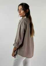 Blusa color beige con cuello mao, mangas 3/4 con puños elásticos y detalle de diseño geométrico texturizado en el frente.