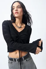 Top tejido negro con trama calada, escote en V, frunce central regulable y mangas acampanadas.