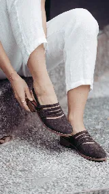 Zueco de cuero marrón chocolate con múltiples tiras cruzadas en el empeine, talón descubierto con tira trasera y suela plana con pequeño taco.
