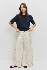Pantalón de jean wide leg color beige con pequeños bordados y estampados coloridos dispersos, de tiro medio y corte amplio en las piernas.