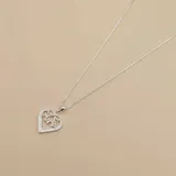 Conjunto de collar y dije de corazón calado en plata 925 con circonias. El dije tiene la palabra "MAMA" y un moño.