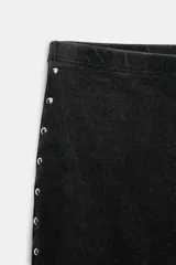 Pantalón de tiro medio con cintura elástica y corte acampanado. Presenta un acabado lavado y detalle de tachas metálicas a lo largo de las costuras laterales.