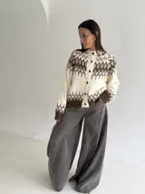 Cardigan de punto con diseño jacquard de inspiración nórdica, en tonos blanco, gris y marrón. Presenta cuello redondo, cierre frontal con botones y mangas largas con puños acanalados.