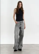 Pantalón de jean de corte wide leg en color gris lavado, con diseño de tiro medio y cierre frontal con botón y cremallera.