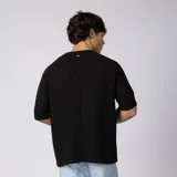 Remera oversize de lino entramado color blanco off-white, con cuello redondo, mangas cortas de hombro caído y etiqueta aplicada en el borde inferior.
