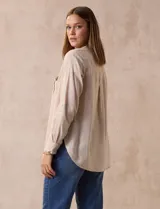 Blusa color beige de lino, marca Dash. Cuello a la base, escote en V y abertura con botones. Delantera con bolsillos. Largo de manga regulable con presilla y botón.