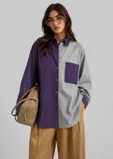 Camisa oversize de diseño bicolor, combinando paneles en color violeta y gris. Presenta cuello clásico, cierre frontal con botones, bolsillo en el pecho y mangas largas con puños abotonados.