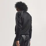 Campera deportiva Adidas Originals color negro, con cierre frontal, cuello alto, puños y cintura acanalados. Presenta las icónicas tres tiras blancas en las mangas y el logo del trébol bordado en el pecho.