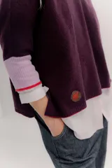 Buzo de punto en color negro con mangas tres cuartos y puños en contraste color marrón. Presenta un diseño holgado con tajos laterales y un aplique circular con logo en la parte inferior.