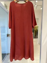 Vestido midi de lino color terracota, con escote en V, mangas tres cuartos y corte amplio y fluido con bolsillos laterales.