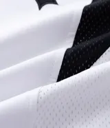 Remera de manga corta en tejido sintético color blanco, con cuello redondo y diseño de estilo deportivo. Presenta estampado frontal con lettering gótico y detalles laterales en tejido microperforado.