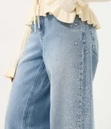 Pantalón wide leg de tiro bajo confeccionado en jean de algodón, con cierre frontal y aplicación de brillos y tachas en los laterales.