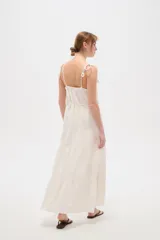 Vestido largo de algodón color blanco, con tirantes finos ajustables con lazos en los hombros, escote recto decorado con apliques florales tridimensionales, cordón ajustable en la cintura y falda larga con volados horizontales.