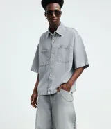 Pantalón de jean estilo baggy balloon, de corte holgado con volumen en las piernas y cintura fija con trabillas. Presenta costuras a contratono y detalle de cadena metálica lateral.