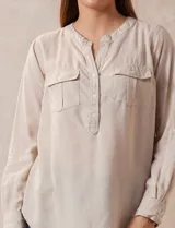 Blusa color beige de lino, marca Dash. Cuello a la base, escote en V y abertura con botones. Delantera con bolsillos. Largo de manga regulable con presilla y botón.