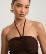 Mono largo de estilo Aladim, color marrón oscuro, con escote halter y busto fruncido. El pantalón es ancho y termina ajustado en los tobillos.