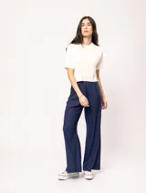 Pantalón de lino color beige, de tiro alto, pierna ancha y levemente acampanada. Tiene pinzas delanteras, elástico en la pretina trasera, cierre delantero y broche interno, bolsillos laterales y dobladillo invisible.